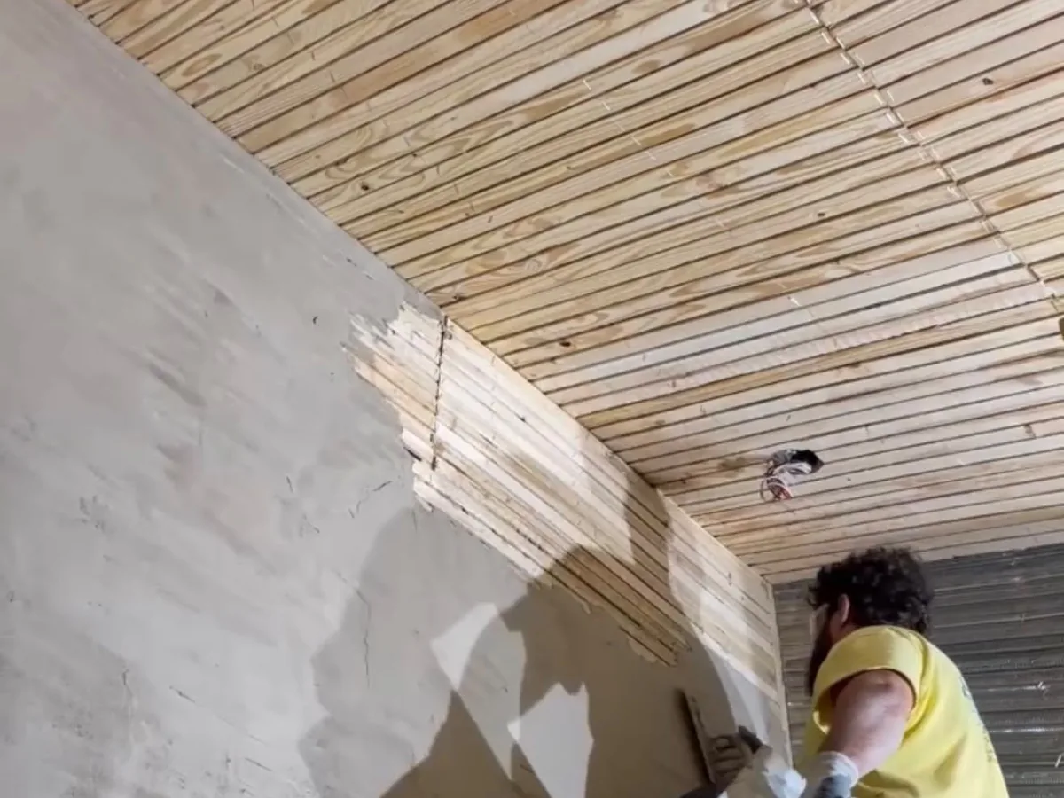 Plasterer working a fresh coat up to a wood slat ceiling detail