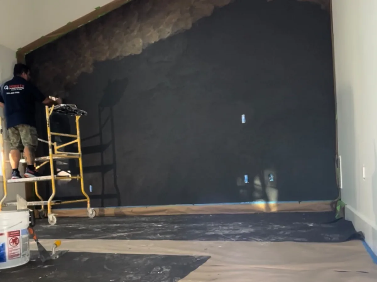 Dark plaster feature wall being finished, floor covered and materials staged
