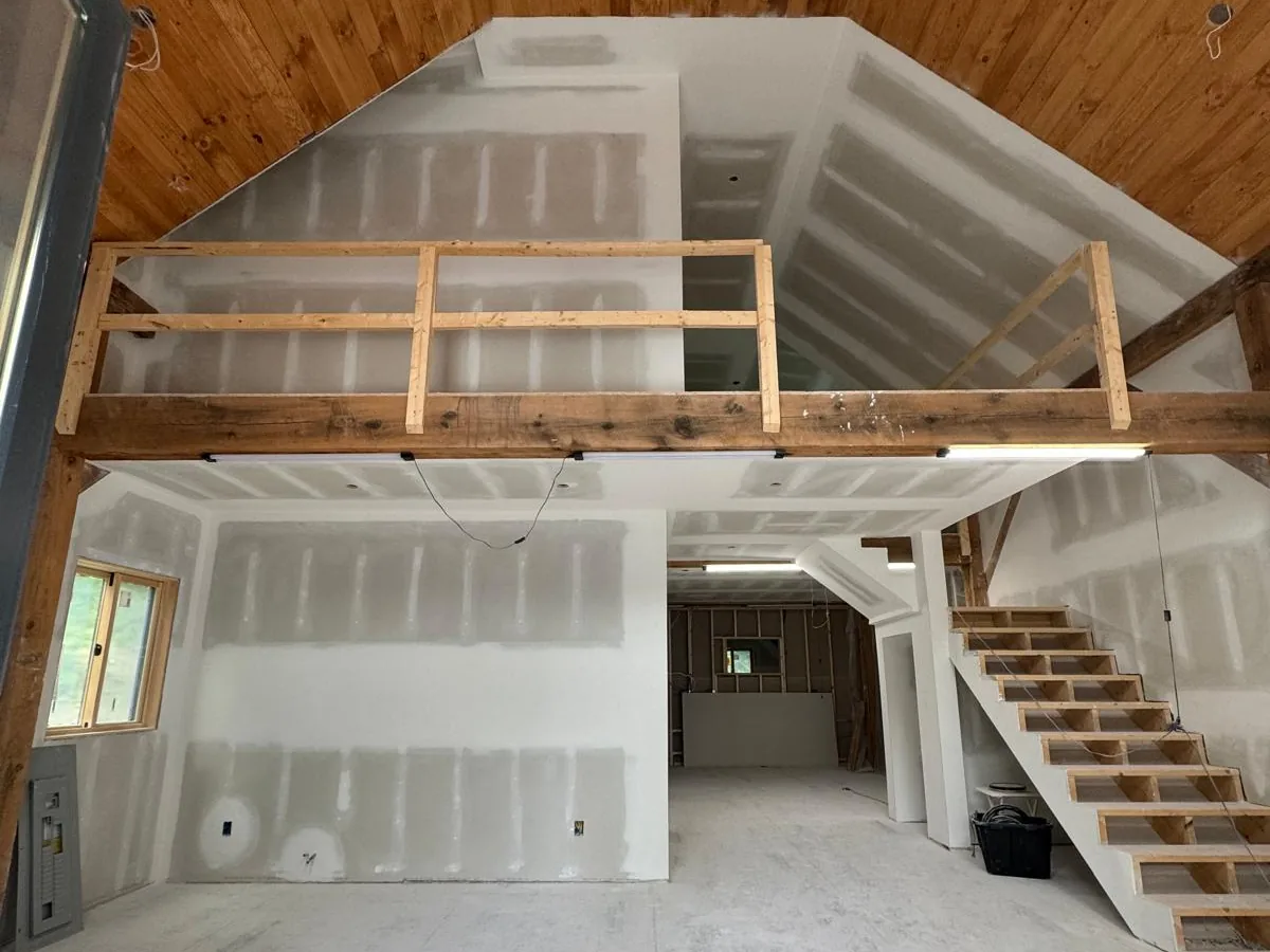 Timber frame barn interior with drywall hung and taped between the posts, mezzanine above