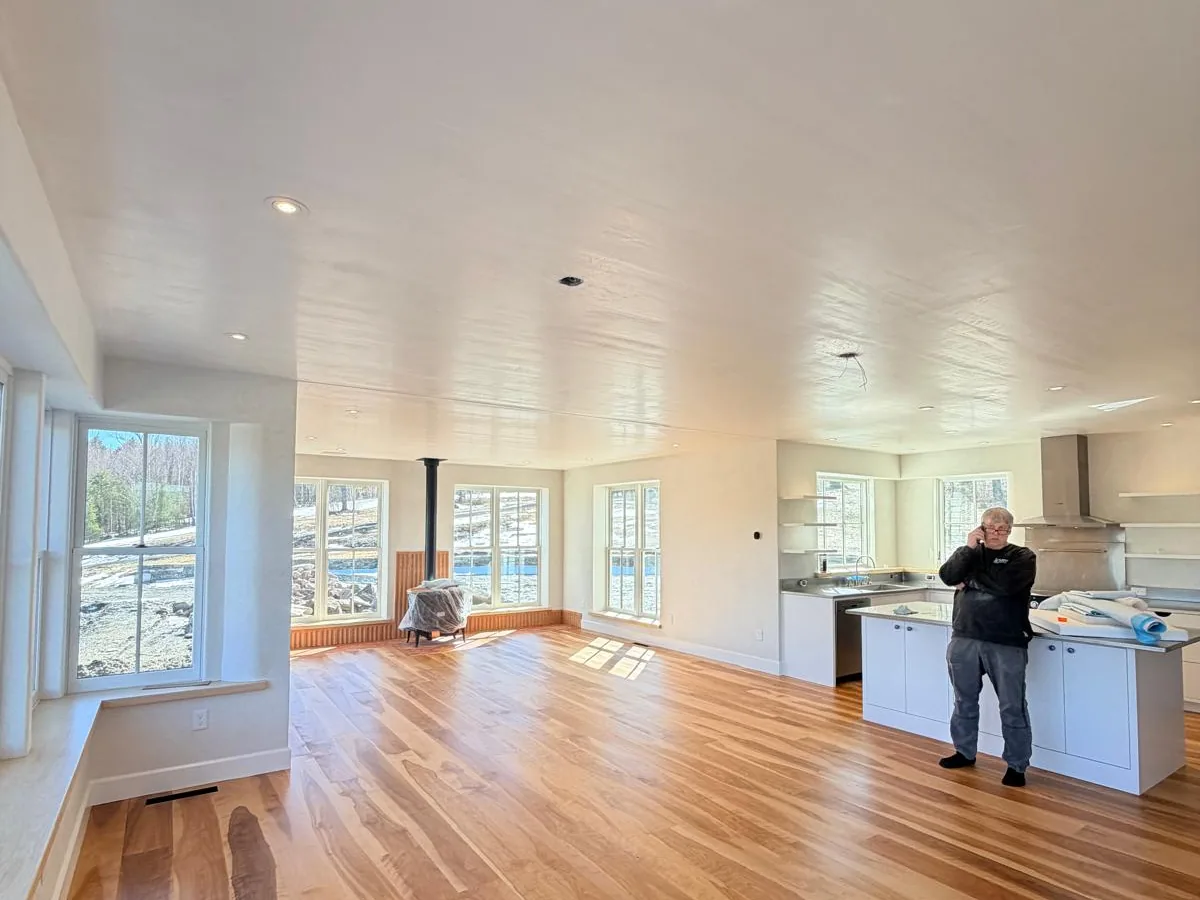 Finished open plan living room with white walls, wood floor and a wood stove
