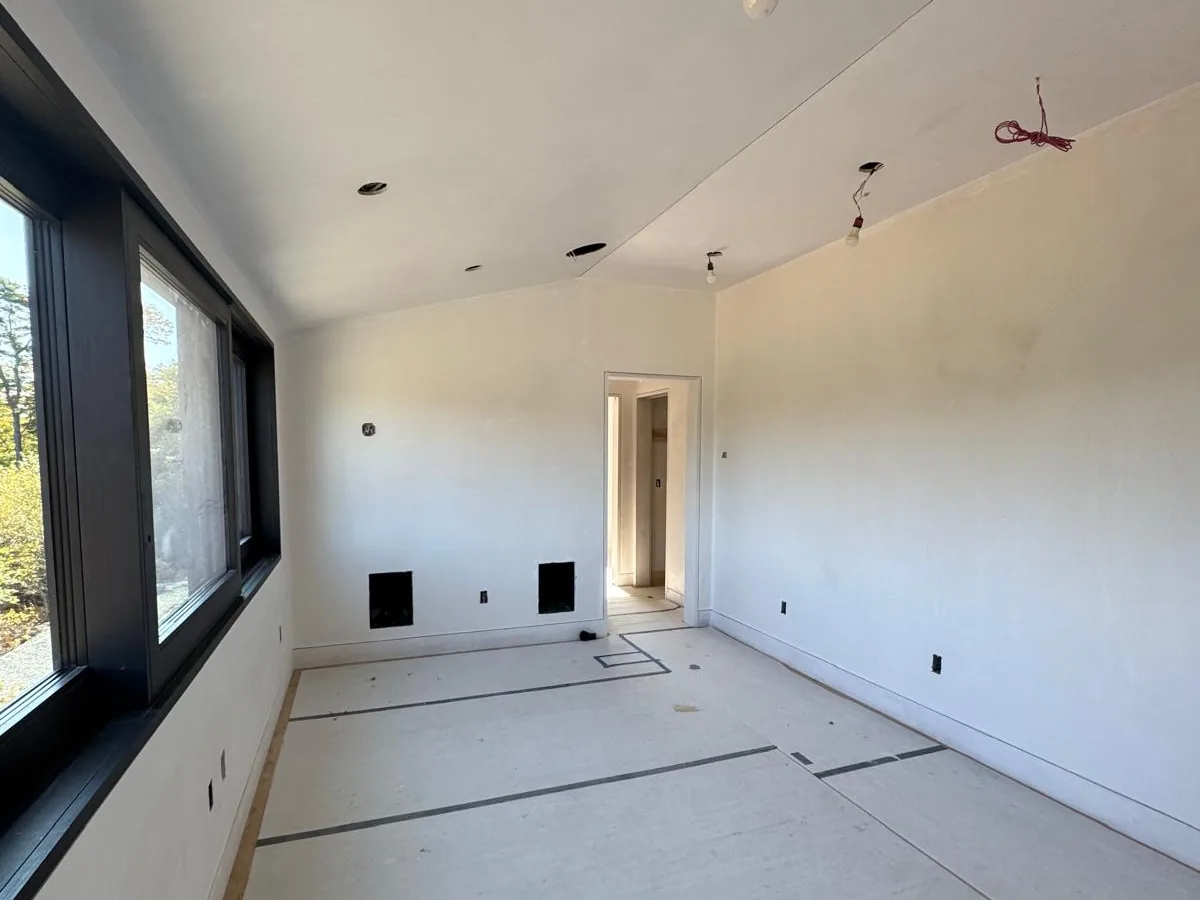 Long finished room with smooth plaster walls, a sloped ceiling and dark framed windows