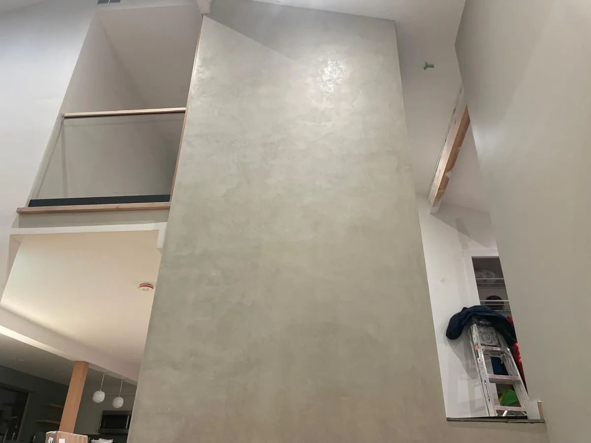 Microcement chimney column rising past the mezzanine in a modern open plan living space
