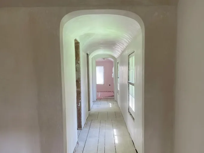 Barrel vaulted hallway plastered smooth, looking through to a pink room at the end