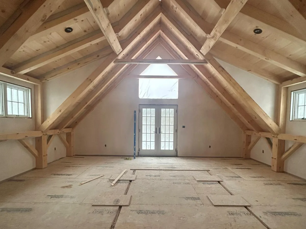 Large plastered attic room under an exposed truss roof with french doors at the gable