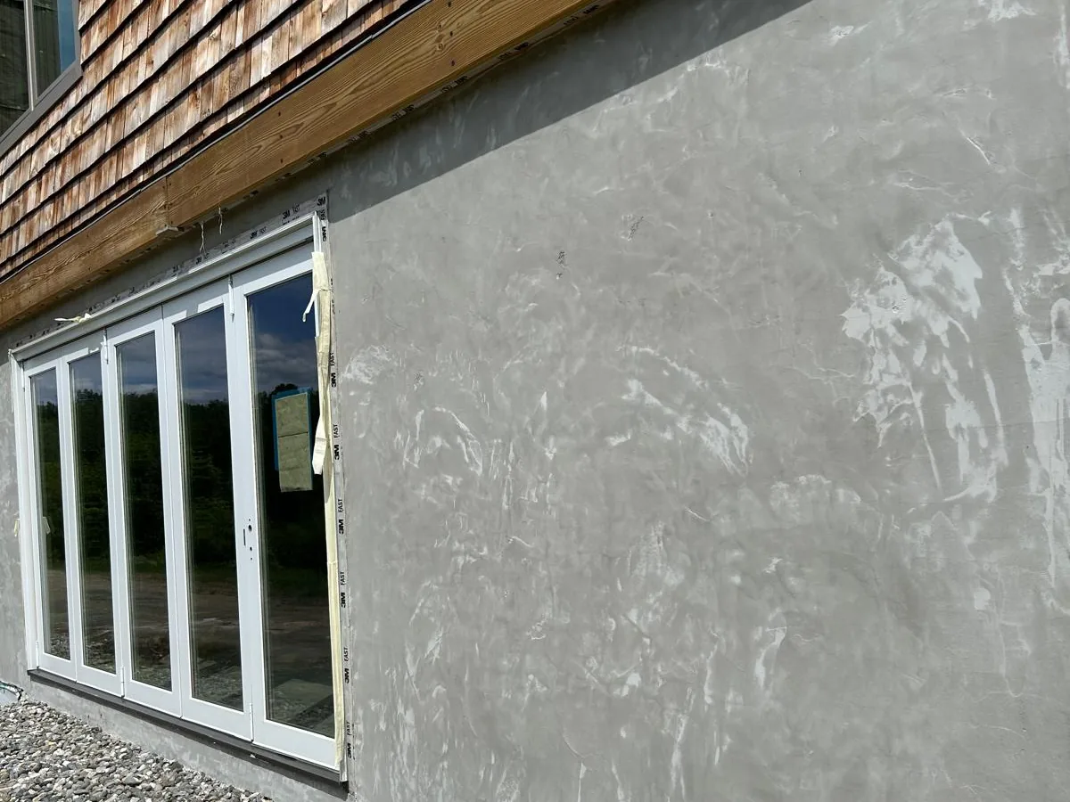 Stucco base coat applied to the walkout level of a shingled house