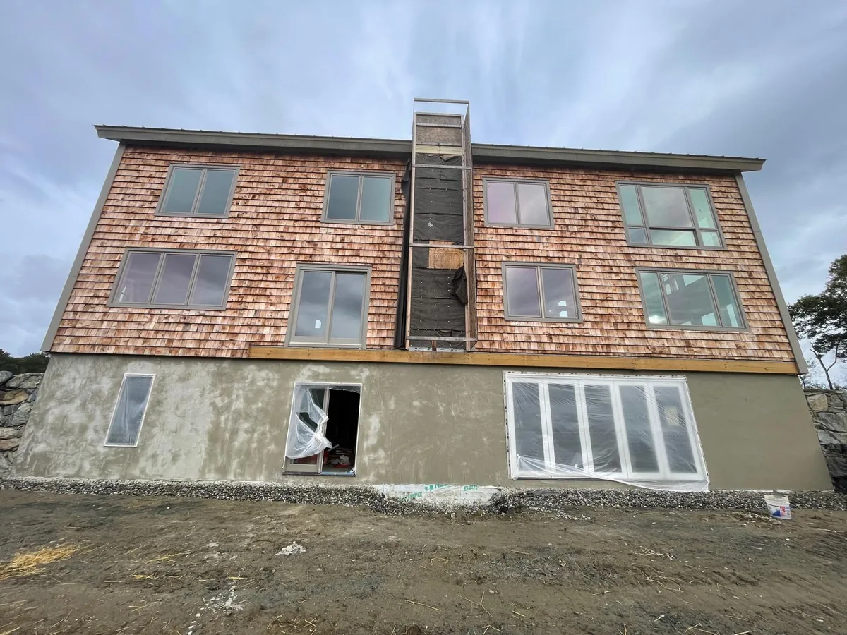 Rear elevation of a large shingled house with the lower level stucco base coated
