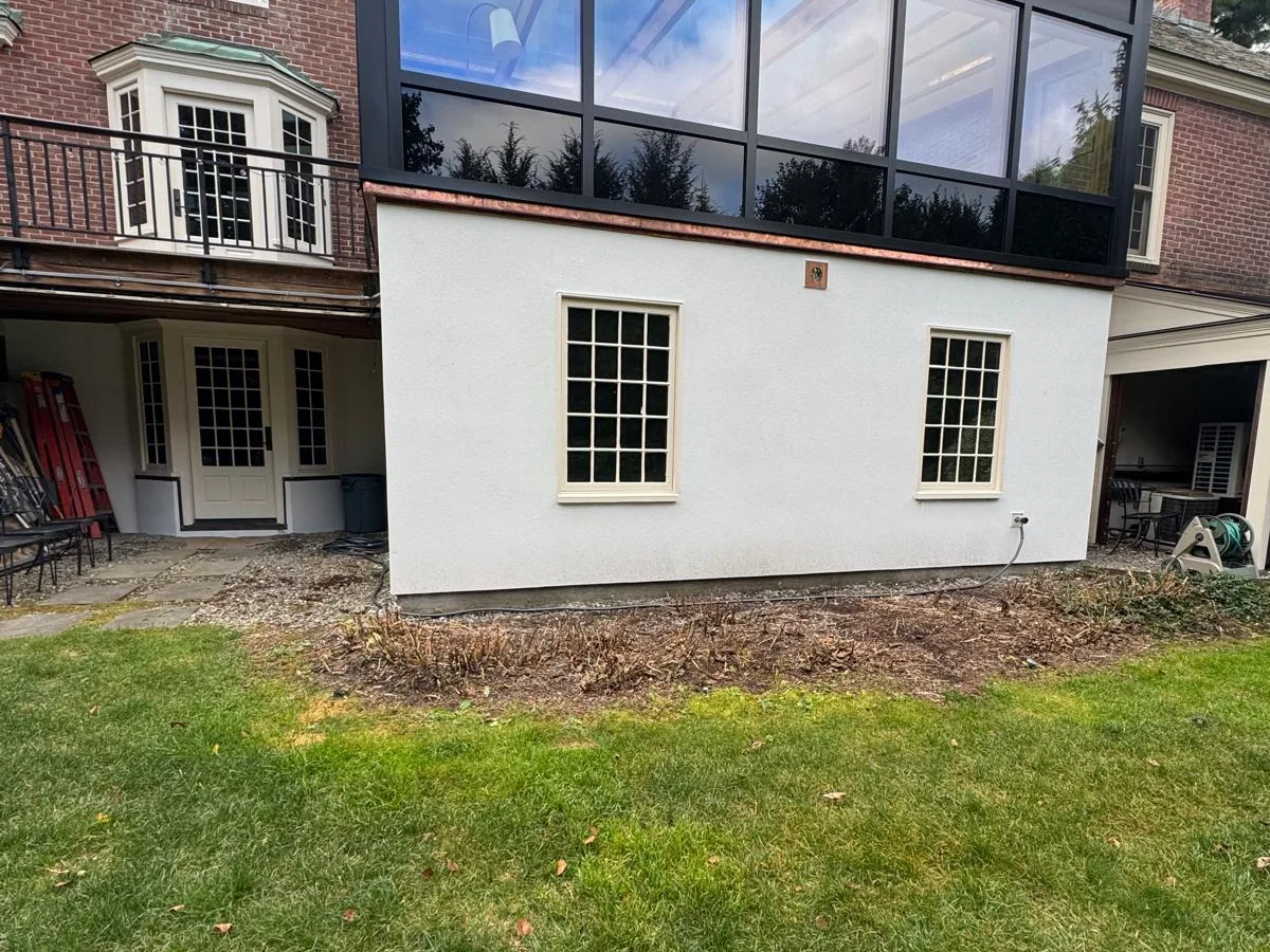 Finished white stucco on the lower level of a brick house with a modern glass addition