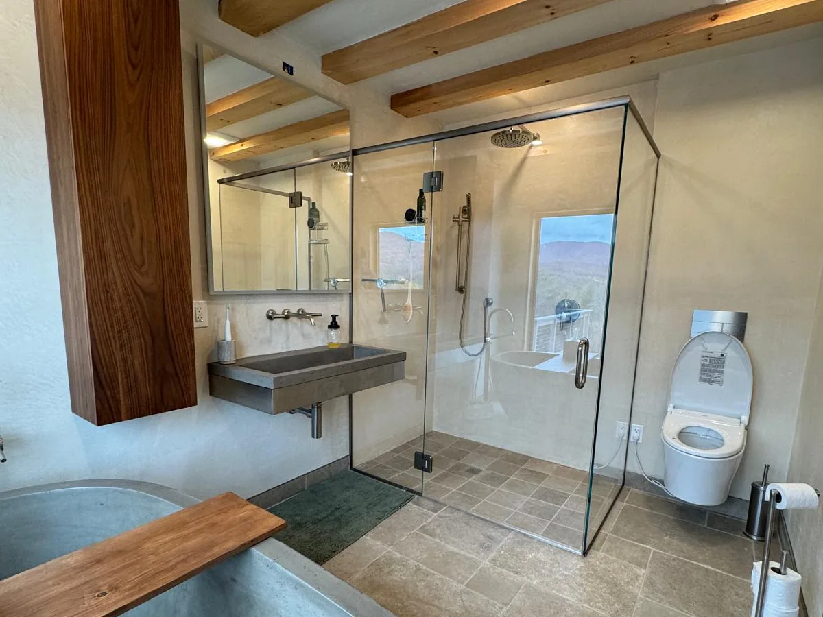 Finished bathroom with tadelakt walls, a plastered soaking tub and a glass walk in shower under timber beams