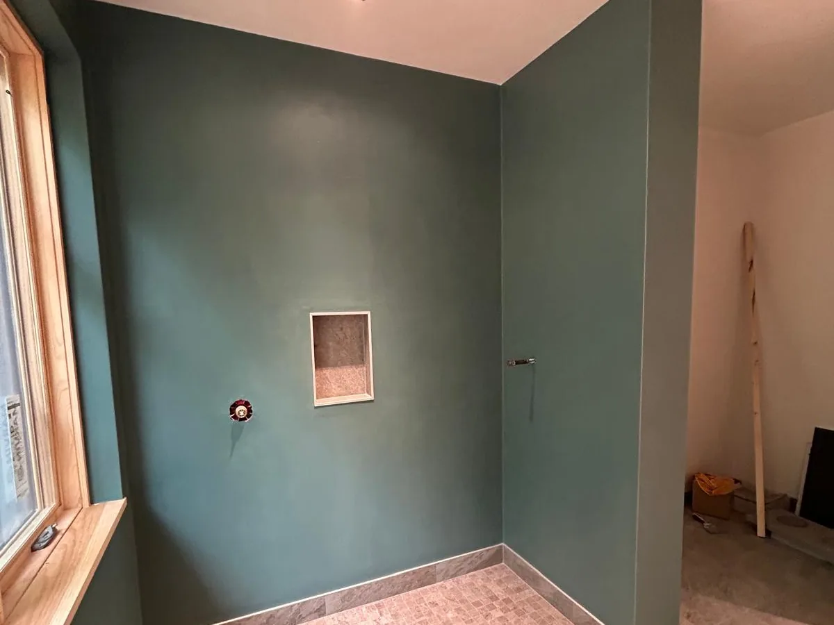 Deep green tadelakt walls being finished in a wet room with a niche and a marble floor
