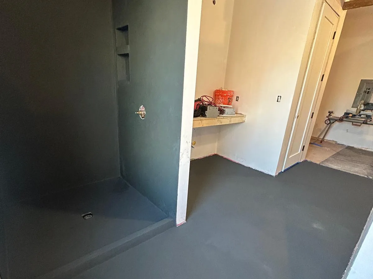 Dark grey tadelakt shower walls flowing into the plastered floor as one continuous surface, mid project