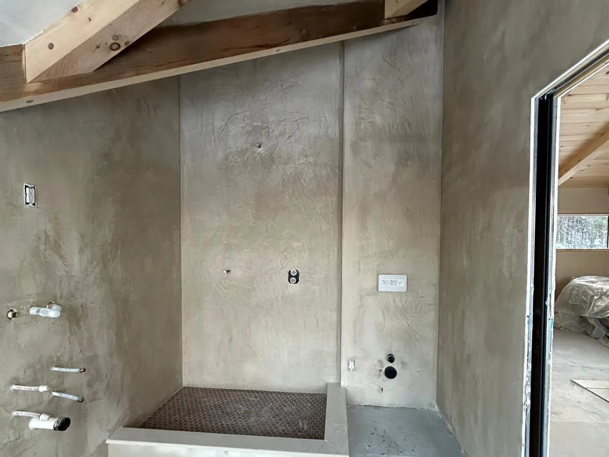 Grey plastered wet room with a built in bench and a tiled shower pan, near completion