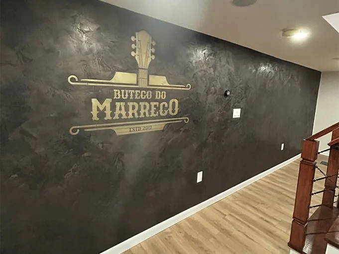 Black burnished Venetian plaster feature wall in a finished basement bar, with a custom gold logo applied over the plaster