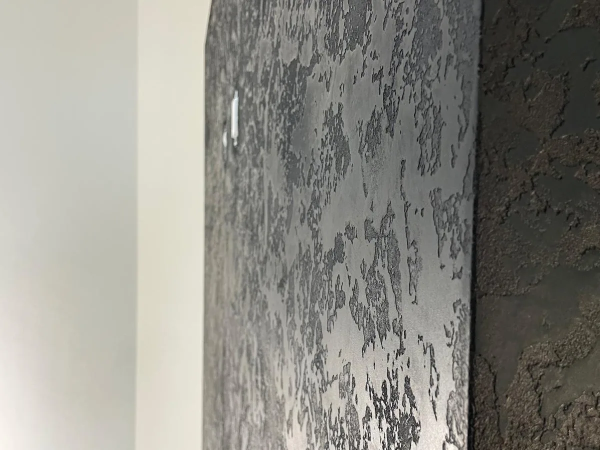 Close view of a dark textured Venetian plaster wall with a marble like relief pattern catching the light