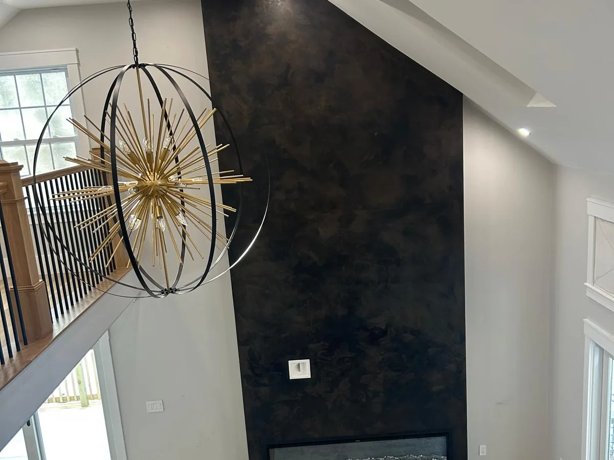 Dark Venetian plaster fireplace surround rising two storeys in a living room with a chandelier and wood floor