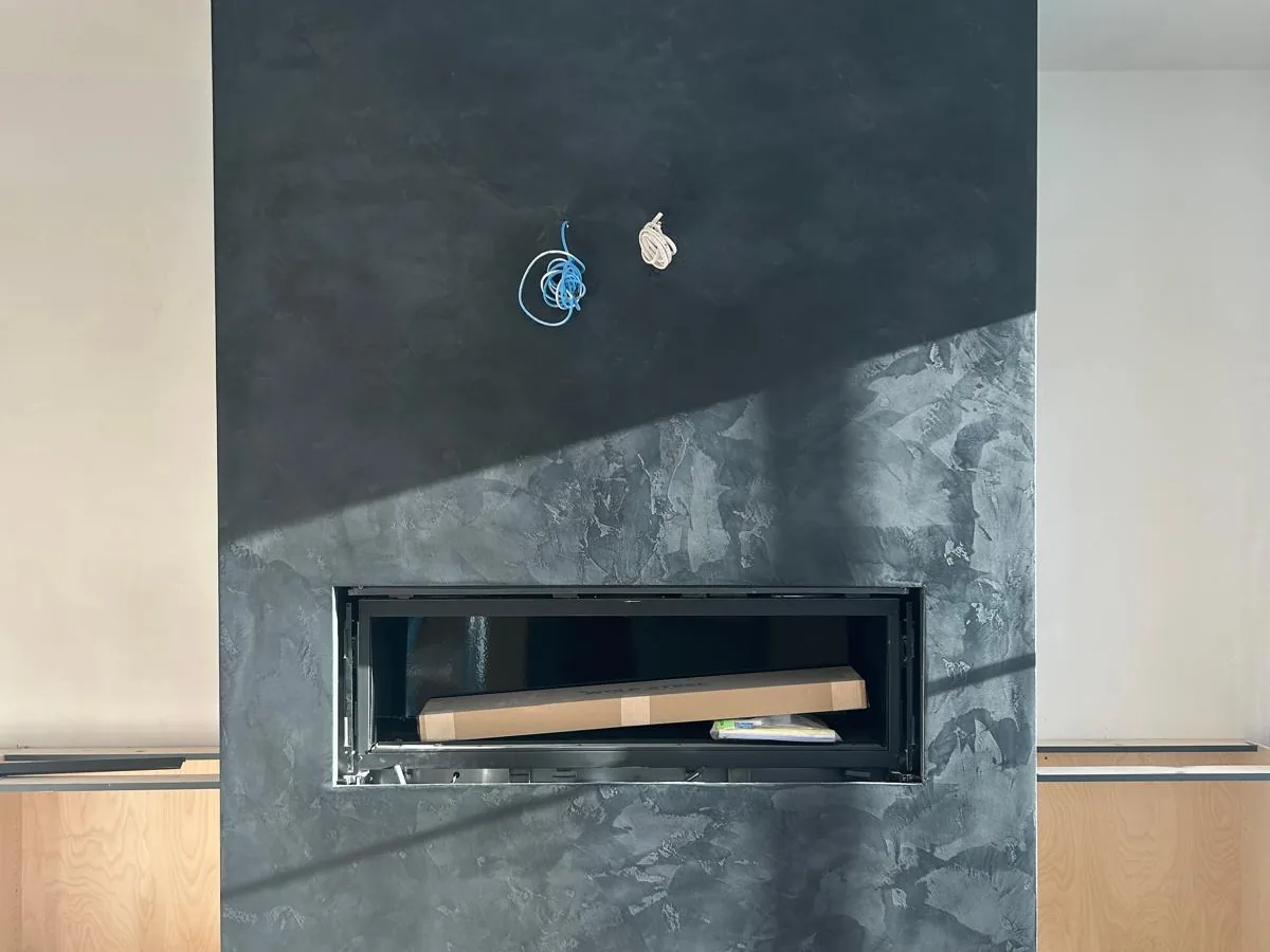 Charcoal Venetian plaster fireplace with a linear gas insert, mid installation in a bright living room