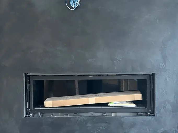 Charcoal Venetian plaster wall built around a linear fireplace opening, mid installation