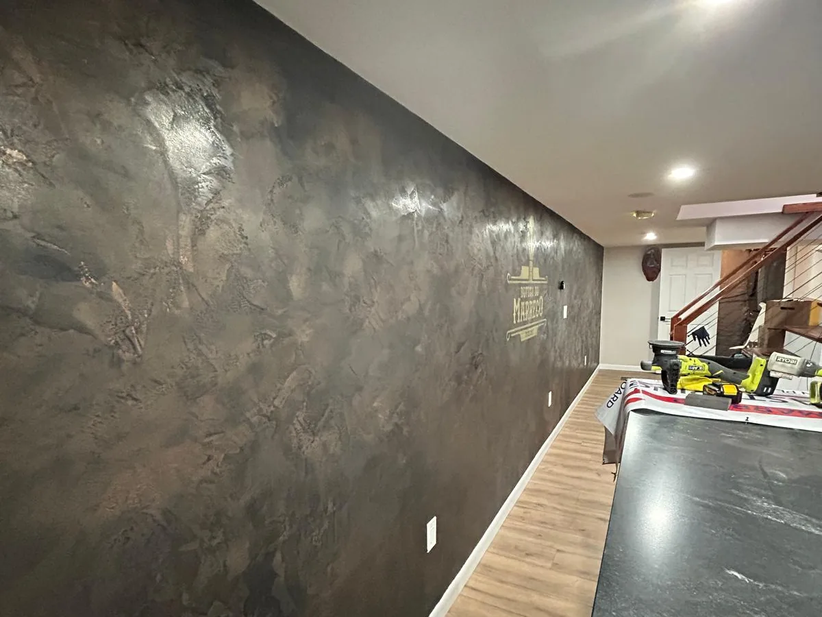 Dark mottled Venetian plaster running the length of a bar wall with a stone counter